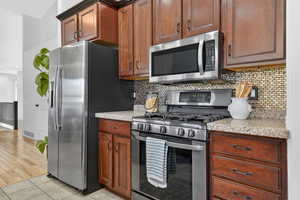 Kitchen featuring appliances with stainless steel finishes, decorative backsplash, light tile  floors, and brown cabinets