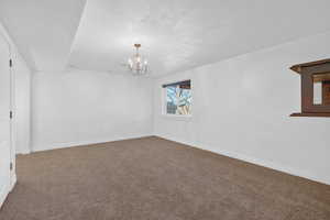 Empty room featuring a chandelier, a textured ceiling, and carpet flooring