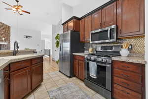 Kitchen featuring appliances with stainless steel finishes, light granite counters, a ceiling fan, light tile patterned flooring, and tasteful backsplash