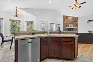 Kitchen featuring dishwasher, an island with sink, dark brown cabinetry, a fireplace, and open floor plan