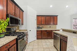 Kitchen with stainless steel appliances, Gas Range light tile tile floors, backsplash, light stone counters, and recessed lighting