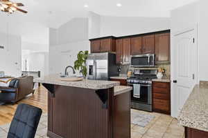 Kitchen featuring stainless steel appliances, open floor plan, an island with sink, dark brown cabinets, and a breakfast bar