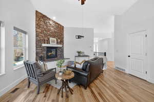 Living area featuring high vaulted ceiling, light wood finished floors, a stone fireplace, and plenty of natural light
