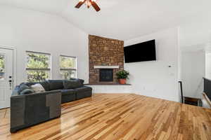 Living area with light wood finished floors, ceiling fan, a fireplace, and high vaulted ceiling
