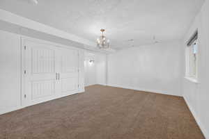 Unfurnished bedroom with carpet flooring, a textured ceiling, a closet, and a chandelier