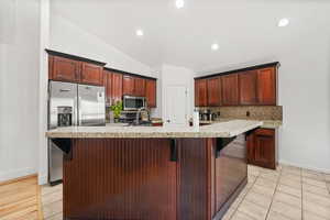 Kitchen featuring a kitchen bar, tasteful backsplash, stainless steel appliances, lofted ceiling, and light stone countertops