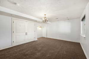 Unfurnished bedroom featuring dark colored carpet, a textured ceiling, a closet, and a chandelier