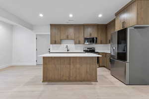 Kitchen featuring stainless steel appliances, recessed lighting, a center island, light wood-style floors, and brown cabinetry