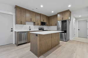 Kitchen with appliances with stainless steel finishes, recessed lighting, light wood-style flooring, a center island, and light stone counters