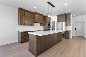 Kitchen featuring hanging light fixtures, a kitchen island with sink, stainless steel appliances, light wood-style flooring, and recessed lighting