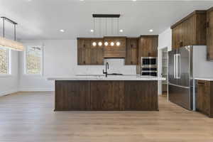 Kitchen with a center island with sink, pendant lighting, recessed lighting, light wood-type flooring, and dark brown cabinets