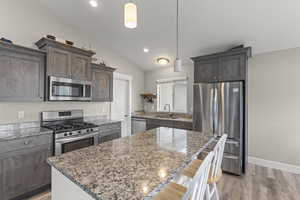 Kitchen with stainless steel appliances, hanging light fixtures, LVP flooring and large granite island.