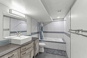 Bathroom featuring tiled shower / bath combo, vanity, a textured wall, and a textured ceiling