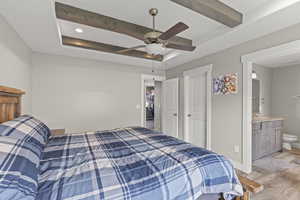Bedroom with wood finished floors, ensuite bathroom, a ceiling fan, beam ceiling, and a raised ceiling