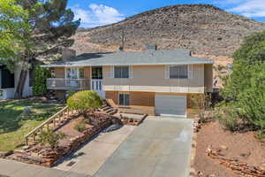 Single story home with a chimney, brick siding, concrete driveway, an attached garage, and a mountain view