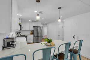 Kitchen featuring light stone countertops, freestanding refrigerator, recessed lighting, light wood finished floors, and hanging light fixtures