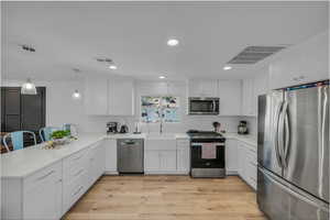 Kitchen featuring appliances with stainless steel finishes, decorative light fixtures, light wood finished floors, white cabinets, and recessed lighting