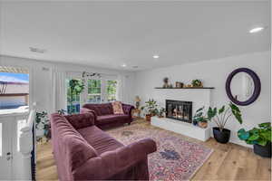 Living room featuring light wood-style floors, a glass covered fireplace, and recessed lighting