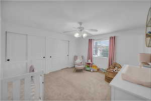 Bedroom featuring a nursery area, light colored carpet, a closet, and a ceiling fan