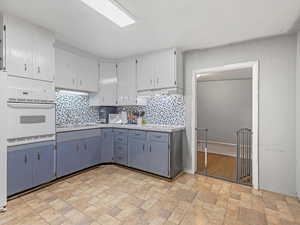 Kitchen featuring white/blue cabinets, backsplash, oven, and light countertops