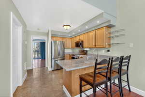 Kitchen featuring stainless steel appliances, a breakfast bar, a peninsula, light stone countertops, and recessed lighting