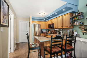 Kitchen with appliances with stainless steel finishes, recessed lighting, a kitchen breakfast bar, light stone countertops, and a peninsula