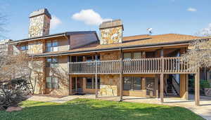 Back of house featuring a chimney, a balcony, a yard, and stone siding