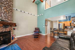 Living room featuring dark wood-style floors, a fireplace, ceiling fan, and a towering ceiling