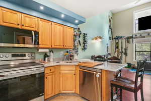 Kitchen featuring appliances with stainless steel finishes, light stone countertops, a peninsula, and a breakfast bar