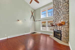 Unfurnished living room featuring high vaulted ceiling, a baseboard radiator, a stone fireplace, wood finished floors, and ceiling fan