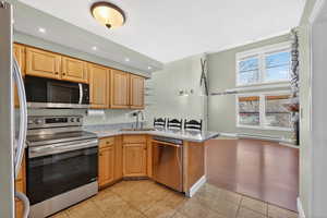 Kitchen featuring stainless steel appliances, a peninsula, light stone countertops, light tile patterned floors, and baseboard heating