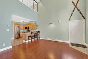 Living area with light wood-style floors, a baseboard heating unit, and a towering ceiling