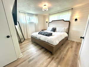 Bedroom with wood walls, wood finished floors, a textured ceiling, and multiple windows