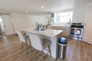 Kitchen featuring stainless steel electric stove, recessed lighting, light wood finished floors, a kitchen breakfast bar, and an island with sink