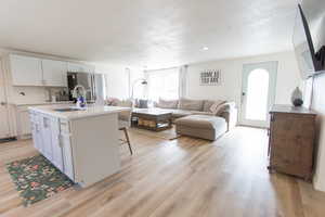 Kitchen featuring white cabinets, open floor plan, stainless steel fridge with ice dispenser, a kitchen island with sink, and light wood-style floors