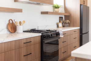 Kitchen with open shelves, gas stove, modern cabinets, freestanding refrigerator, and light stone countertops