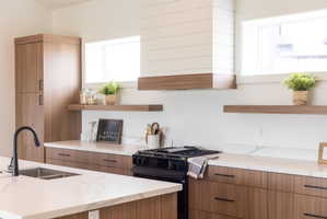 Kitchen featuring open shelves, modern cabinets, light stone counters, black gas range, and two tone cabinets