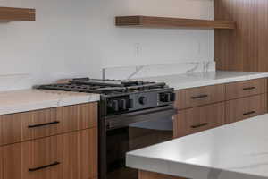 Kitchen featuring black range with gas cooktop, modern cabinets, brown cabinets, light stone counters, and open shelves