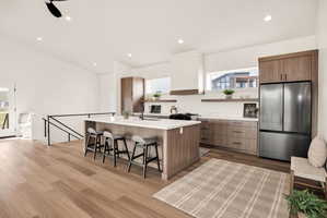 Kitchen with freestanding refrigerator, an island with sink, a breakfast bar area, modern cabinets, and dark wood-style flooring