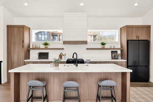 Two tone kitchen with freestanding refrigerator, light stone countertops, recessed lighting, light wood-style floors, and two tone color scheme