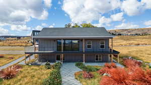 Rear view of house with board and batten siding, a balcony, a shingled roof, and a patio area,landscape in this photo is virtual