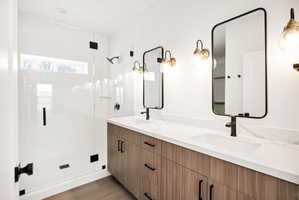 Full bathroom with double vanity, a stall shower, and light wood-type flooring