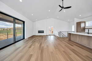 Unfurnished living room with light wood-type flooring, recessed lighting, high vaulted ceiling, ceiling fan, and a fireplace