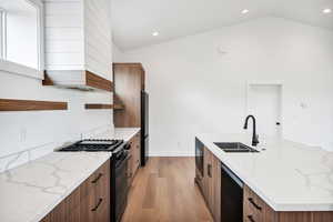 Kitchen featuring brown cabinetry, open shelves, light stone countertops, black appliances, and lofted ceiling