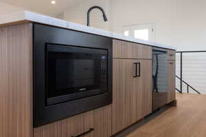 Detailed view of black microwave, modern cabinets, light wood-style floors, stainless steel dishwasher, and recessed lighting