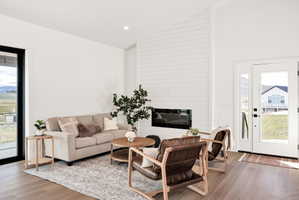 Living room with plenty of natural light, light wood finished floors, vaulted ceiling, a large fireplace, and recessed lighting