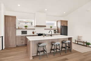 Kitchen with open shelves, a breakfast bar, light wood finished floors, an island with sink, and modern cabinets