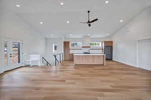 Kitchen featuring open floor plan, a center island with sink, light countertops, recessed lighting, and high vaulted ceiling