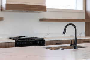 Kitchen with open shelves, custom exhaust hood, black range with gas stovetop, and light stone counters