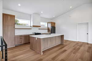 Kitchen with open shelves, light wood-type flooring, recessed lighting, brown cabinetry, and an island with sink